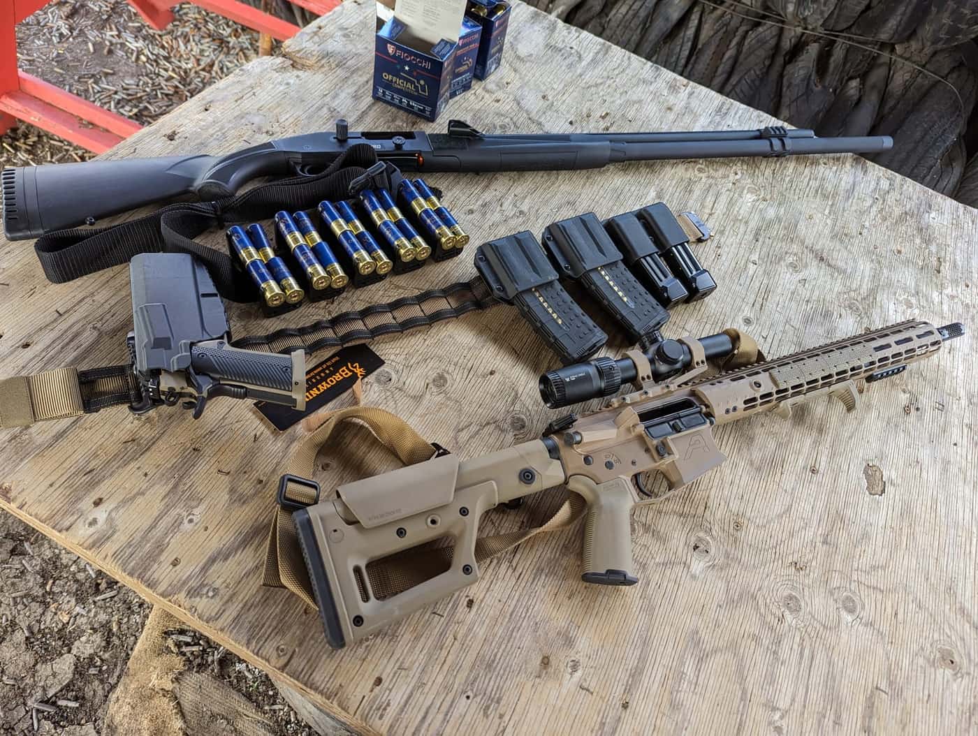A 3-Gun kit laid out on a table: AR with an LPVO, shotgun, pistol in a competition holster, belt and magazines