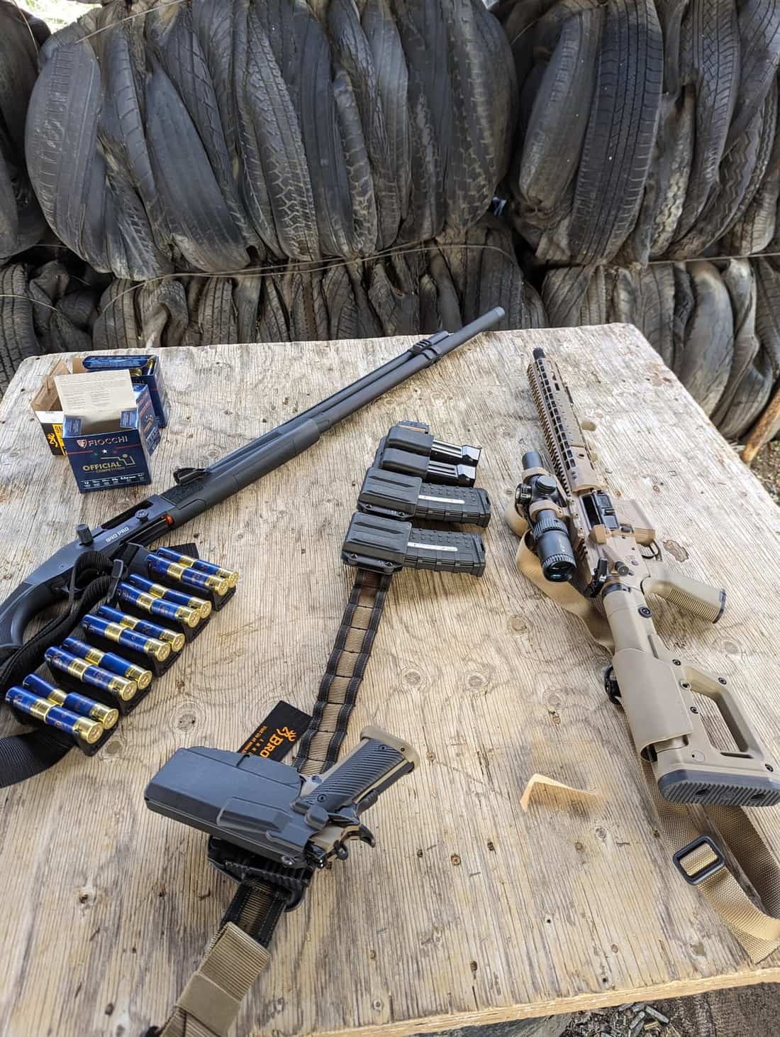 A full 3-Gun kit stood up on a table: semi-auto shotgun, shells, competition belt with caddy, rifle and pistol