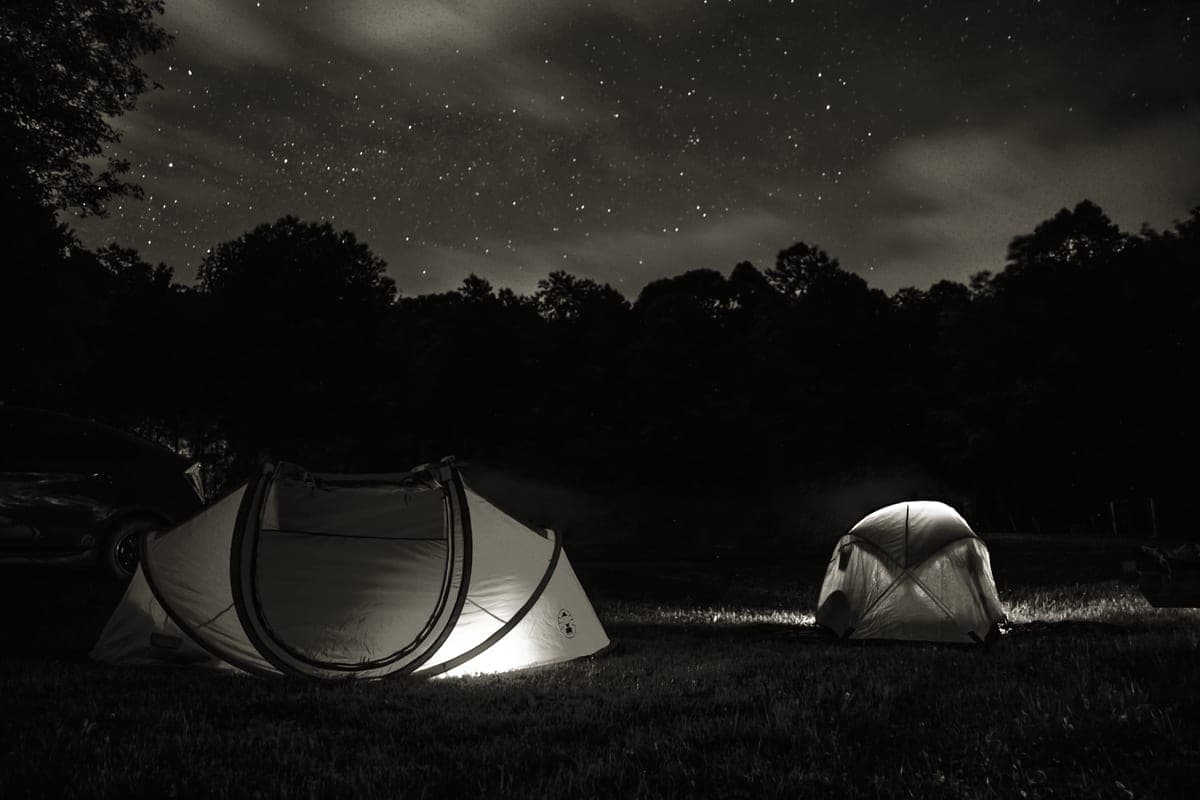 Lit dome tents at a forest campsite after dark