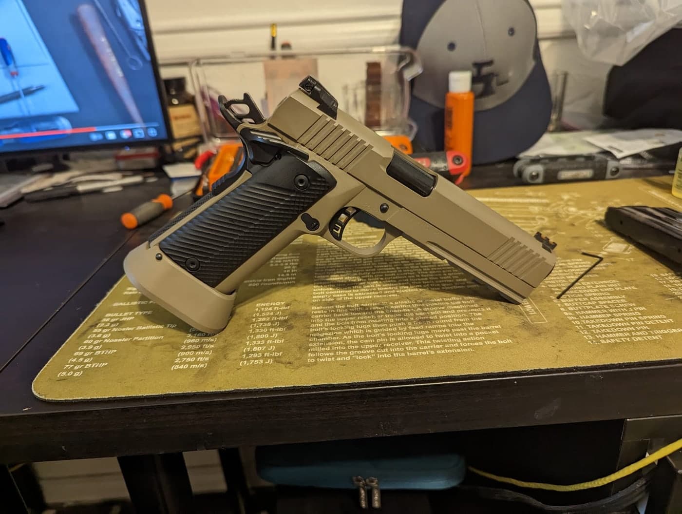The finished tan and black pistol standing upright on the bench, showing the extended magwell and basepad