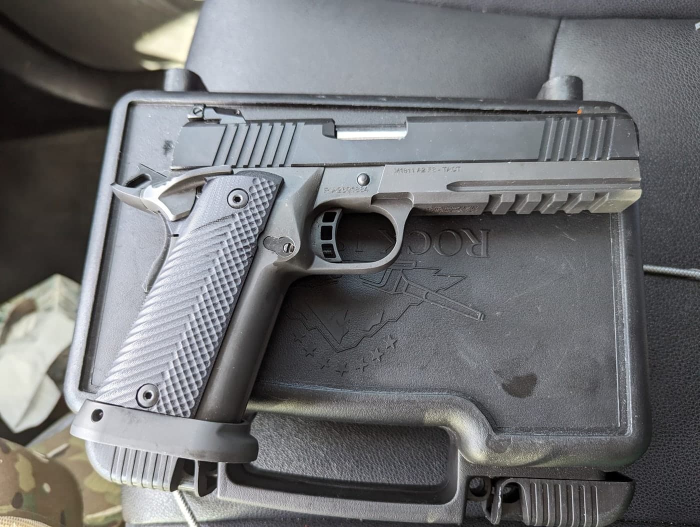 A black double-stack 1911 pistol resting on its factory case