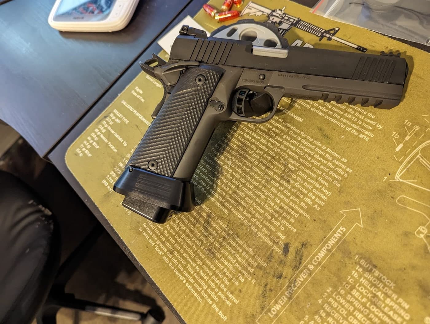 The black double-stack 1911 on a printed gunsmithing bench mat with a magazine inserted