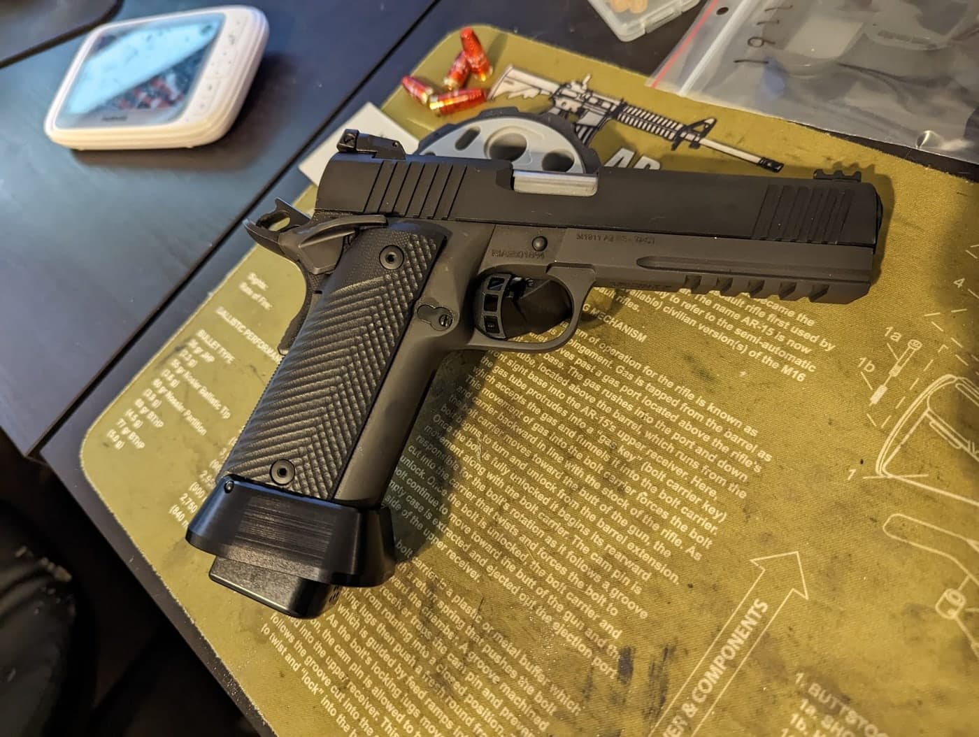 A closer view of the black double-stack 1911 on the bench mat showing the slide serrations and frame