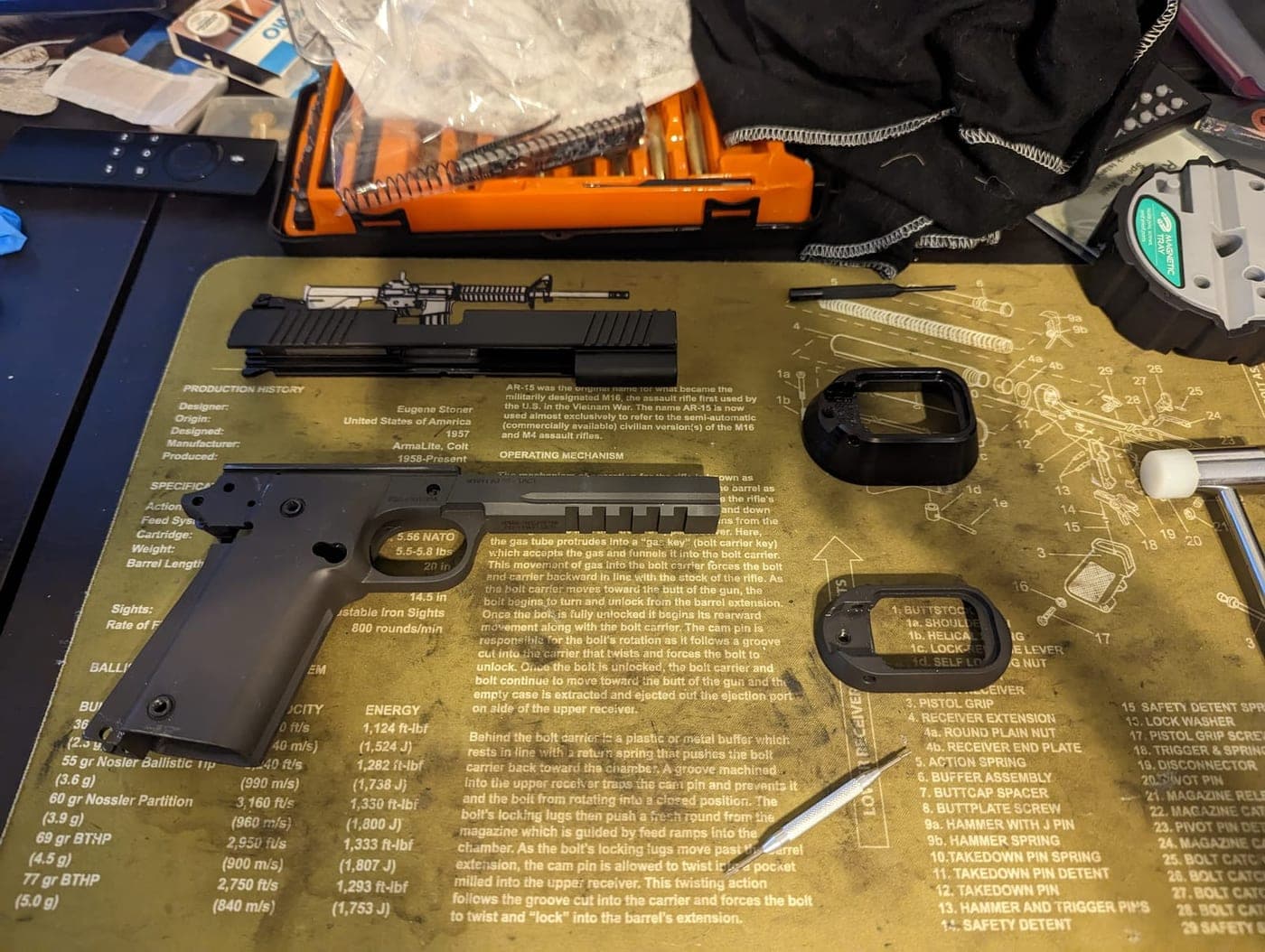 The pistol disassembled into frame, slide, barrel and magwell parts laid out on the bench mat