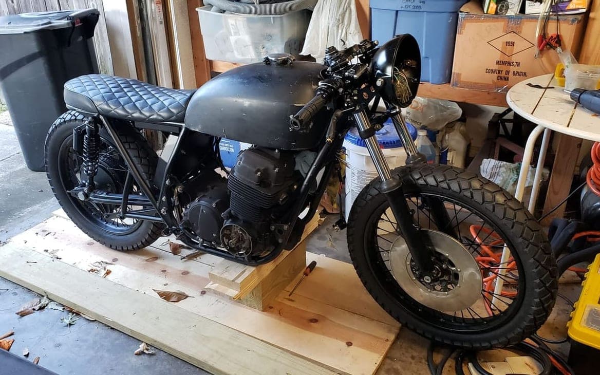 The near-complete CB750 cafe racer standing on boards in the garage, tank, seat, forks and wheels all fitted